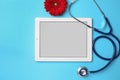 Tablet, flower and stethoscope on light blue background. Gynecological care
