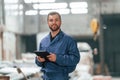 With tablet in hands. Factory worker in blue uniform is indoors