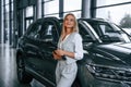 With tablet in hands. Woman in formal clothes is in the car dealership