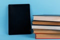 A tablet is located near a pile of books. The concept of knowledge. On a blue background.