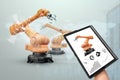 A tablet in a man`s hand controlling robotic arms in a modern factory. Iot technology concept, smart factory. Digital Royalty Free Stock Photo