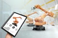 A tablet in a man`s hand controlling robotic arms in a modern factory. Iot technology concept, smart factory. Digital Royalty Free Stock Photo