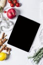 Tablet with a measuring tape, rosemary, nuts, parsley root, tomatoes, cinnamon and red apples on a white wooden background top Royalty Free Stock Photo