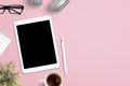 Tablet mockup on pink work desk surrounded with headphones, glasses, notepad, plant, cup of coffee and pen