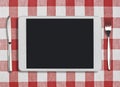 Tablet pc, fork and knife on red checked Royalty Free Stock Photo