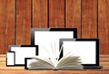 Tablet pc, mobile phone, computer and openned book on wooden tab Royalty Free Stock Photo