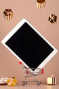 Tablet pc on red mini shop cart trolley and flying gold gift boxes on beige background Royalty Free Stock Photo