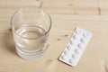 Tablet pills blister and a  glass of water rest on a wooden table with copy space for your text Royalty Free Stock Photo