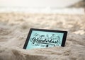 Tablet in sand with black wanderlust doodles against blue background