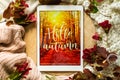 The tablet says the word hello Autumn with red leaves and a dais on the wooden background. Concept of the autumn. View from above. Royalty Free Stock Photo