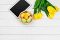 Tablet screen for message and colorful tulips and easter eggs on wooden background