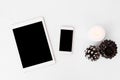 Tablet smartphone christmas composition. stylish arrangement of cones and candle on white background. flat lay top view.