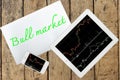 Tablet, smartphone and paper with text bull market on wood table Royalty Free Stock Photo