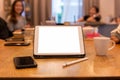 Tablet on table and coffee mug on table with group of friends on dinner table. Royalty Free Stock Photo