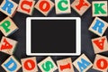 Tablet touchpad with colorful alphabet wooden blocks on black background. Flat lay Royalty Free Stock Photo