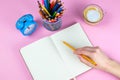 Tablet with white Leaf, next to which is a green plant, a glass with pencils. Hand holds a pen and writes a clock on the sheet in Royalty Free Stock Photo