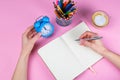 Tablet with white Leaf, next to which is a green plant, a glass with pencils. Hand holds a pen and writes a clock on the sheet in Royalty Free Stock Photo