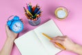 Tablet with white Leaf, next to which is a green plant, a glass with pencils. Hand holds a pen and writes a clock on the sheet in Royalty Free Stock Photo