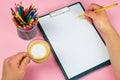 Tablet with white Leaf, next to which is a green plant, a glass with pencils. Hand holds a pen and writes a cup of coffee on the Royalty Free Stock Photo