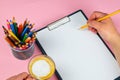 Tablet with white Leaf, next to which is a green plant, a glass with pencils. Hand holds a pen and writes a cup of coffee on the Royalty Free Stock Photo