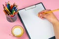 Tablet with white Leaf, next to which is a green plant, a glass with pencils. Hand holds a pen and writes a cup of coffee on the Royalty Free Stock Photo