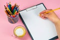 Tablet with white Leaf, next to which is a green plant, a glass with pencils. Hand holds a pen and writes a cup of coffee on the Royalty Free Stock Photo