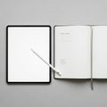 Tablet with a white stylus is placed next to an open notebook on a Royalty Free Stock Photo