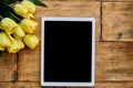 Tablet on wooden table with flowers. Blank screen, copy space for text.