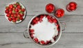 Tabletop photo - large steel pot of strawberries covered with crystal sugar, plate and glass bottles with more fruits around on