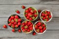 Tabletop view - five small bowls with strawberries, some of them spilled on gray wood desk