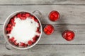 Tabletop view, large steel pot full of strawberries covered with crystal sugar, three bottles of strawberry in syrup next to it on Royalty Free Stock Photo