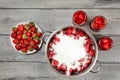 Tabletop view, large steel pot with strawberries covered in crystal sugar, three flasks with fruit in syrup and plate next to it. Royalty Free Stock Photo