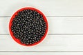 Tabletop view, red ceramic bowl full of freshly harvested blackcurrants, on white boards desk. Royalty Free Stock Photo