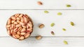 Tabletop view, small bowl with red Turkish pistachios, more nuts scattered on white board desk Royalty Free Stock Photo