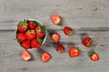 Tabletop view - small ceramic bowl of strawberries, more cut fruits lying around on gray wood desk