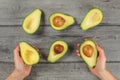 Tabletop view, woman hands holding avocado cut in half, seed visible, more avocados halves on gray wood desk around Royalty Free Stock Photo