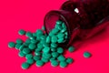 Tablets with Arthrospore or spirulina poured out of a dark glass bottle on a red background