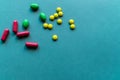 Tablets and caplets on cyan blue background, yellow, green and orange pills on top left corner of the photo, vitamins to