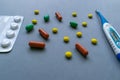Tablets, caplets and thermometer on light gray background, yellow, green and orange pills on top right corner of the