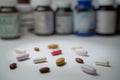 Tablets and capsule pills lay in front of blurry bottles on white background. Royalty Free Stock Photo