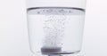 Tablets Falling and Dissolving into a Glass of Water against White Background Royalty Free Stock Photo