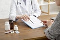 Tablets and medication to patient. Adult woman doctor in white coat shows to put signature in tablet on wooden table Royalty Free Stock Photo