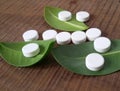 White tablets and green leaves over wooden background symbolizing homeopathy.