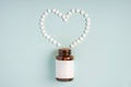 Tablets or pills from a glass jar on a blue background lie in the form of a heart, pharmaceutical medical concept