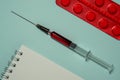 Tablets in red blister packs, glass syringe with red liquid and notepad
