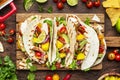 Taco party. Corn tortillas with grilled chicken fillet, salsa sauce, mango, cilantro and red onion on rustic wooden cutting board