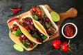 Tacos with steak, tomatoes, onion and cilantro. Top down view serving board on a dark background.