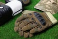 Tactical gloves, camouflage cap and camping lantern on green grass, closeup. Military training equipment