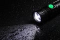 Tactical waterproof flashlight with waterdrops on black background