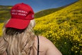 Taft, California - March 25, 2019: Blonde woman wearing a Donald Trump Make America Great Again hat, sitting in a field of yellow
